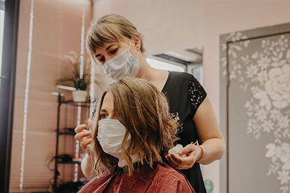 Coiffeuse effectuant un soin capillaire. Cliente et coiffeuse portent un masque chirurgical.